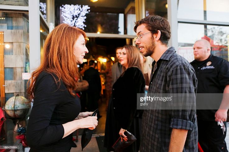 a woman in a black dress and a man in a plaid shirt are talking on the sidewalk in front of a globe. there are other people in the background.