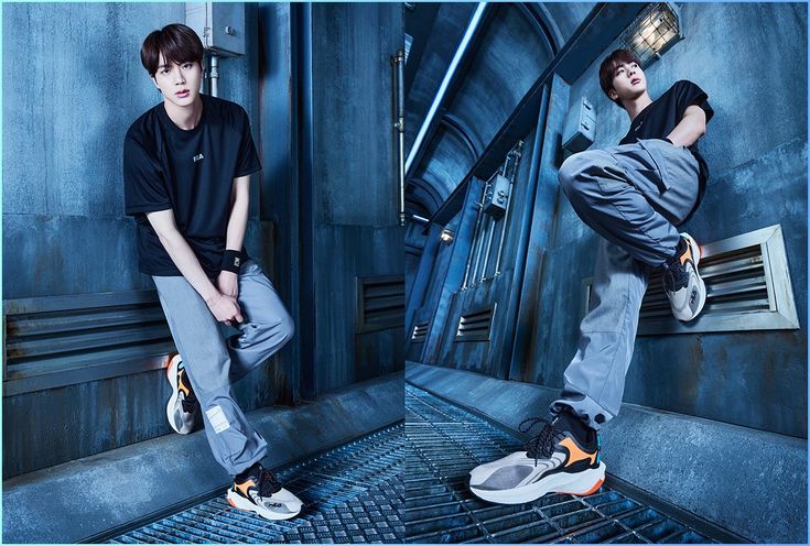 a young asian man poses for a photoshoot in an industrialstyle setting. he wears a black tshirt, grey sweatpants, and white sneakers with orange and black accents. the background features bluetoned metal walls and grated flooring. the lighting is artificial and creates a dramatic and stylish atmosphere.