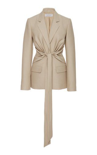 the image is of a beige blazer with a tie waist. the blazer is long sleeved, collared, and has a draped effect at the waist.