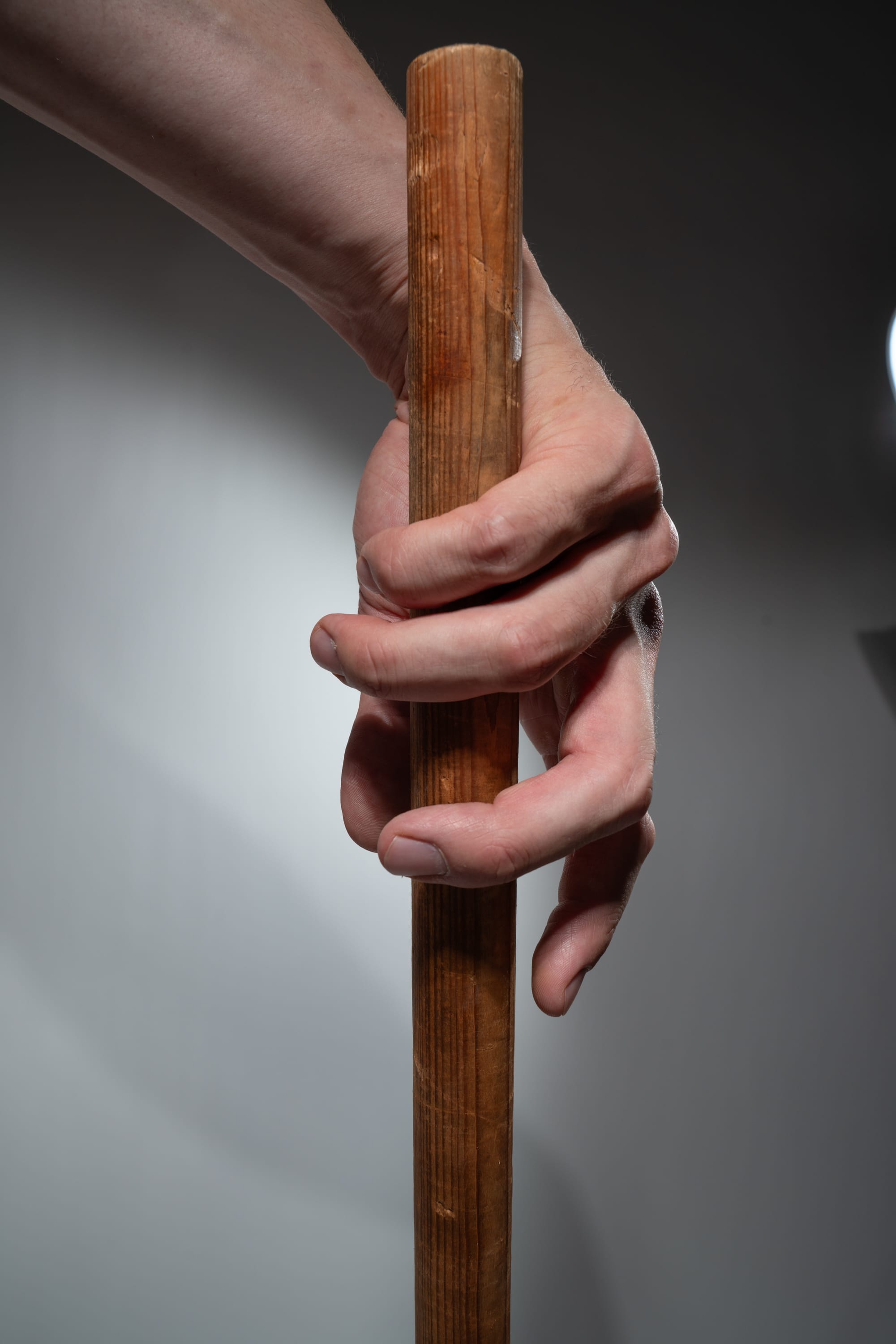 a closeup image of a man's hand tightly gripping a wooden stick. the stick is smooth and cylindrical, showing its natural wood grain. the man's hand is strong and firm, highlighting the pressure applied to the stick. the lighting is soft and diffused, creating a subtle contrast and depth. the focus is on the hand and the stick, emphasizing the texture and the action of gripping.