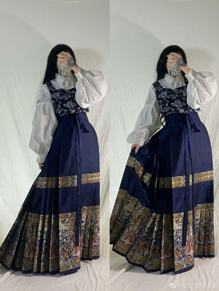 two identical images of a young woman wearing a long, dark blue pleated skirt with a vintagestyle tapestry print along the hem.  she is also wearing a dark floral top under a white puffsleeved blouse. the skirt has a obistyle belt. the style blends gothic lolita and dark academia fashion elements. the model is posing with her hands covering part of her face in both images.  the background is plain white.