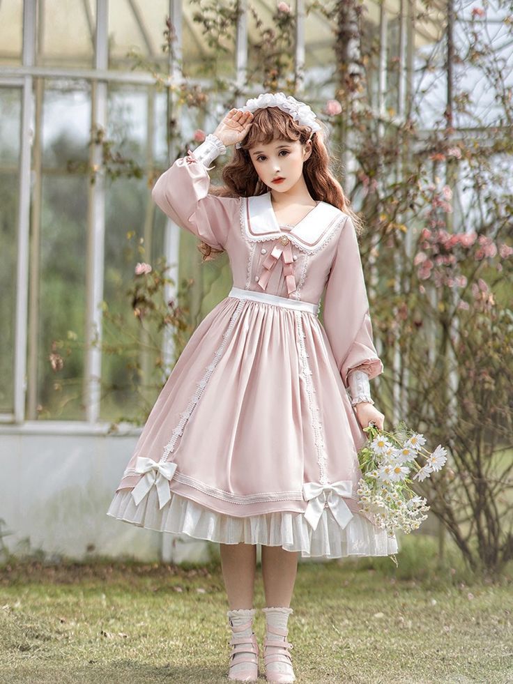 a young woman in a pink and white lolita fashion dress poses in a greenhouse. the soft, natural light highlights the delicate details of her dress and the lush greenery surrounding her. she's holding a bouquet of white flowers.