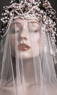 a woman with a veil and headpiece made of pearls and lace covers most of her face. she has on dramatic eye makeup and a soft, romantic lip color. the veil gives a hazy, dreamy effect. the image is mysterious and romantic.