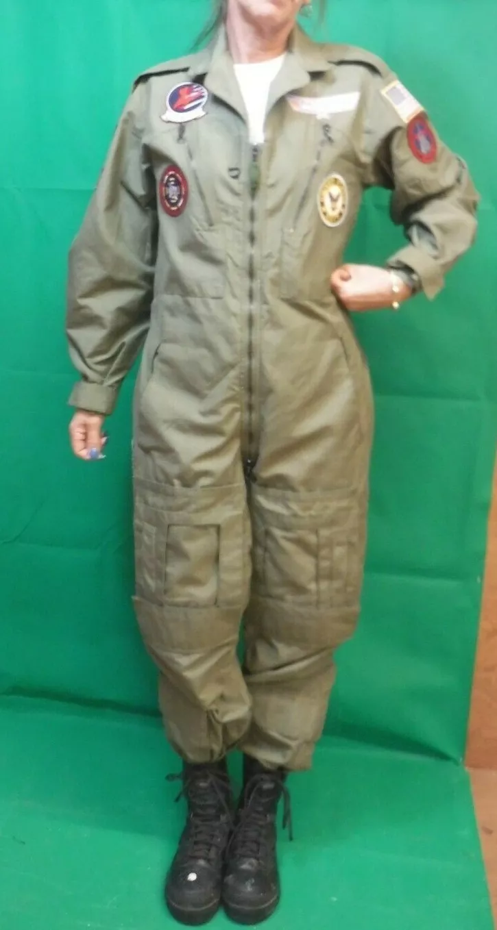 a woman in a green army jumpsuit with zipper and pockets, standing on a green screen, looking at the camera with a neutral expression. she is wearing black boots.