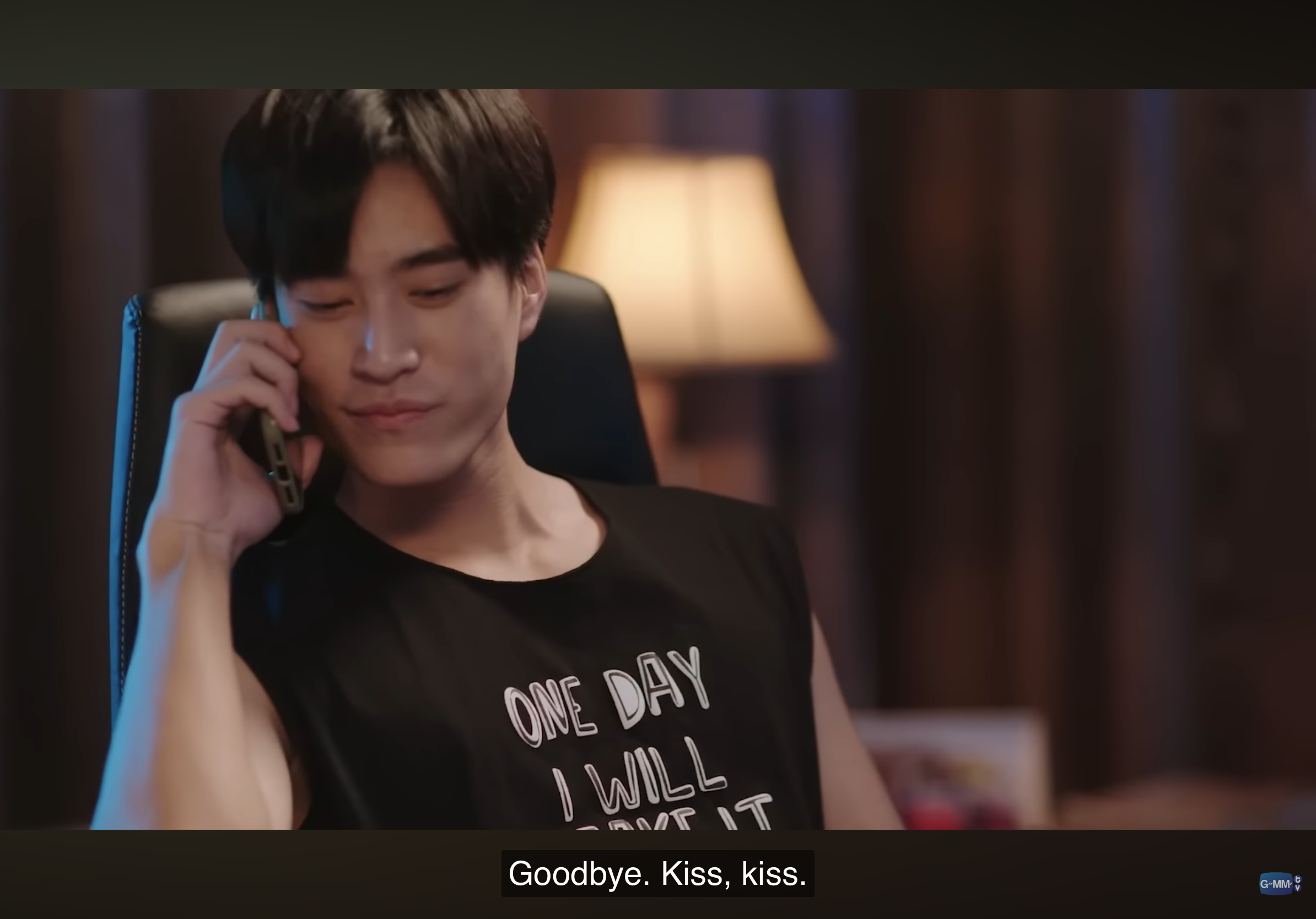 a young man with short black hair is pictured on the phone. he's wearing a black sleeveless shirt with white lettering that reads "one day i will _ _ _ e it" the word "love" is likely covered by his arm. he is smiling and the caption reads: "goodbye. kiss, kiss." the background is out of focus and appears to be a bedroom. the lighting is dim and warm.