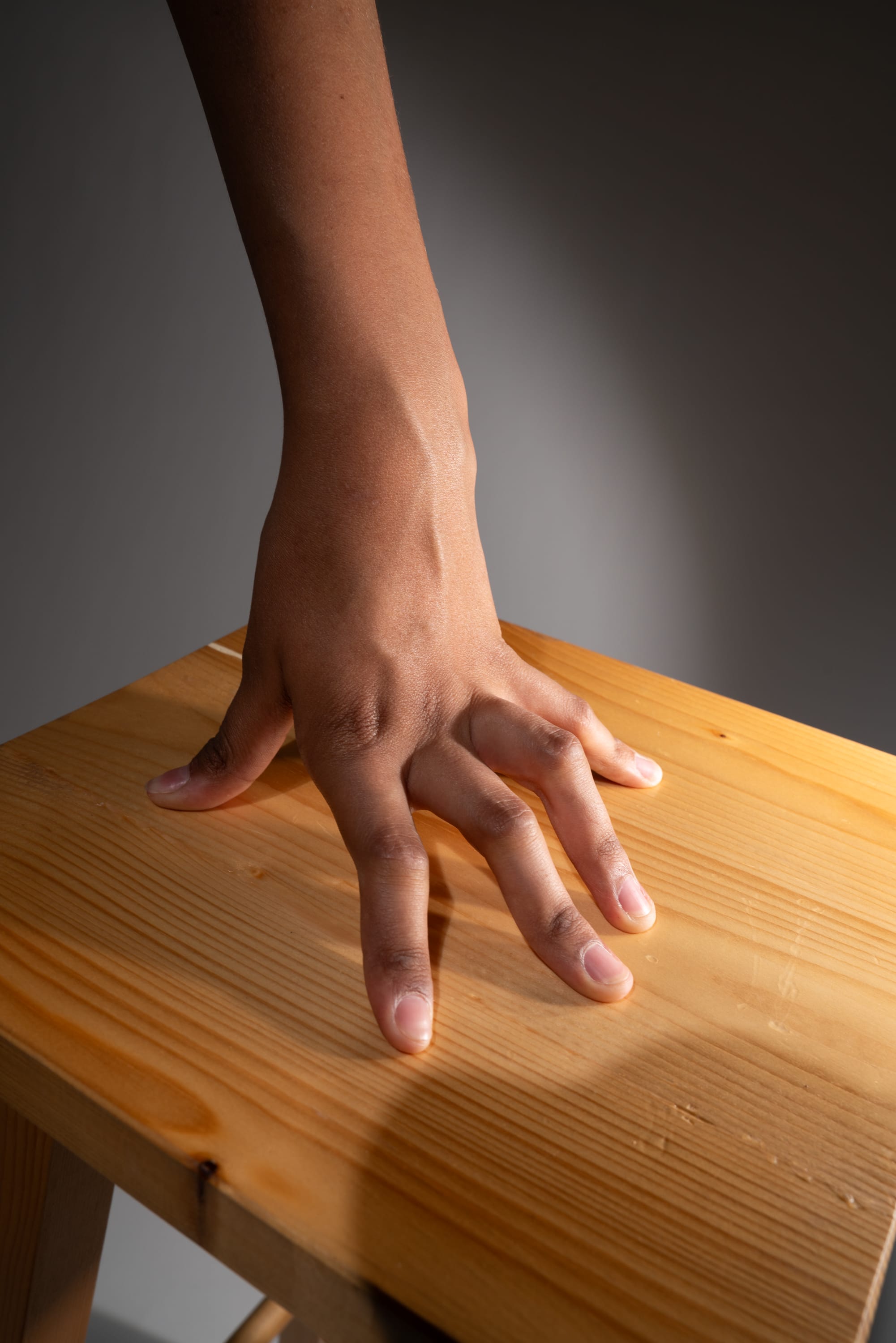 a hand is placed on a wooden stool. the image is lit with studio lighting and taken from a high angle.