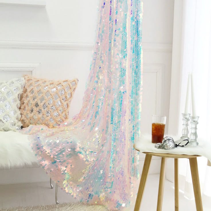 the image shows a room with interior decor. there is a couch with two pillows, one white and one peachcolored. next to the couch is a sequin curtain in iridescent colors. a glass of iced tea, candles, and a table can be seen on the right side of the frame.