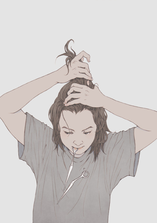 a young woman with brown hair tied up in a messy bun holds a pair of scissors in her mouth.  her head is tilted down as she looks at the scissors, her expression serious and focused. it appears as if she is about to cut her own hair. she is wearing a loosefitting, light grey tshirt. the background is a plain, light grey. the overall tone of the image is neutral and contemplative.