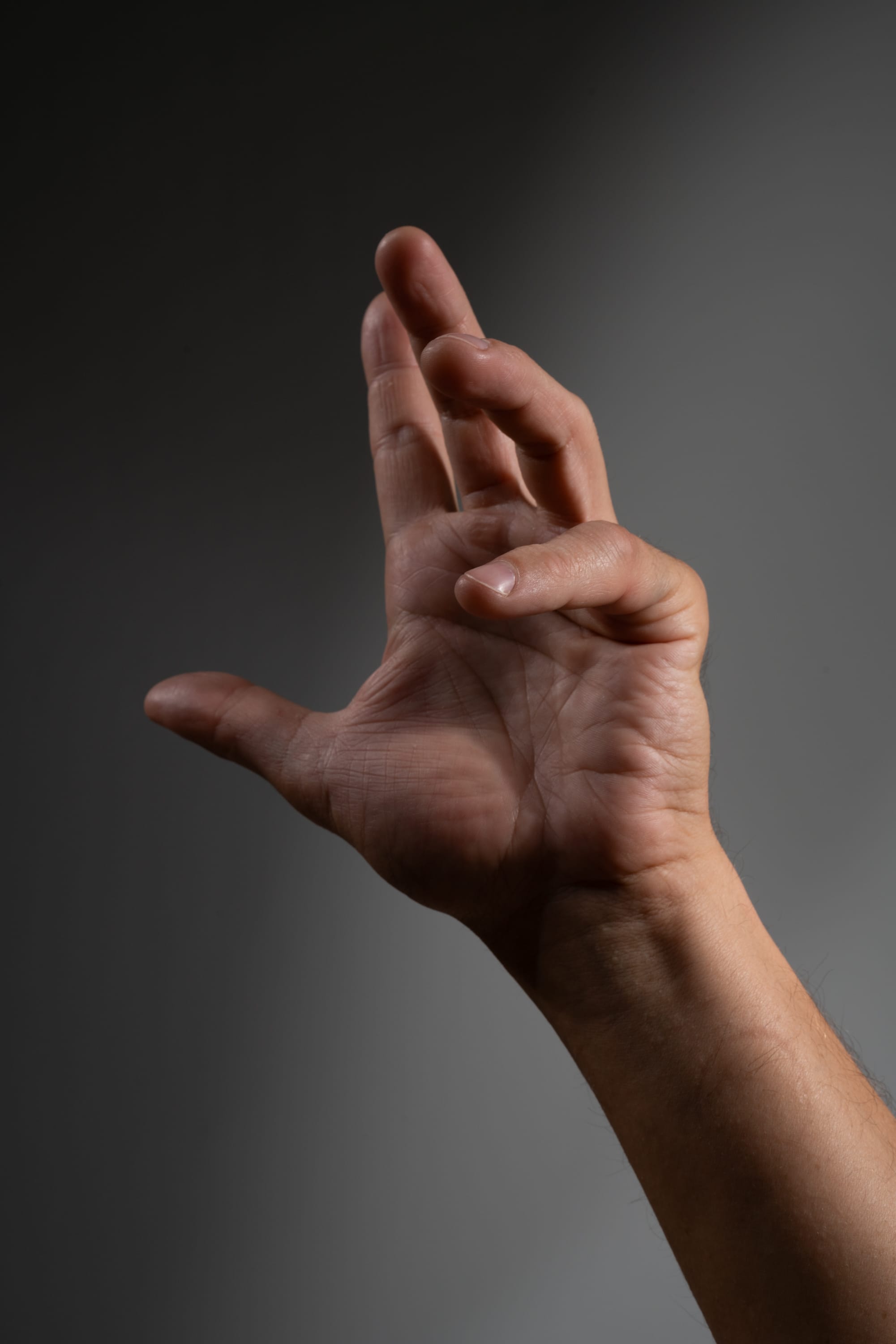 a closeup image of a hand reaching upward against a dark gray background. the lighting is dramatic, casting shadows that highlight the texture of the skin and the shape of the hand. the fingers are slightly curled, suggesting a sense of anticipation or longing.