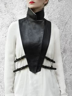 a woman with red lips and a white shirt is wearing a black leather collar with buckles and straps. she is standing in a studio, posing for the camera. the lighting is soft and the image is in focus.