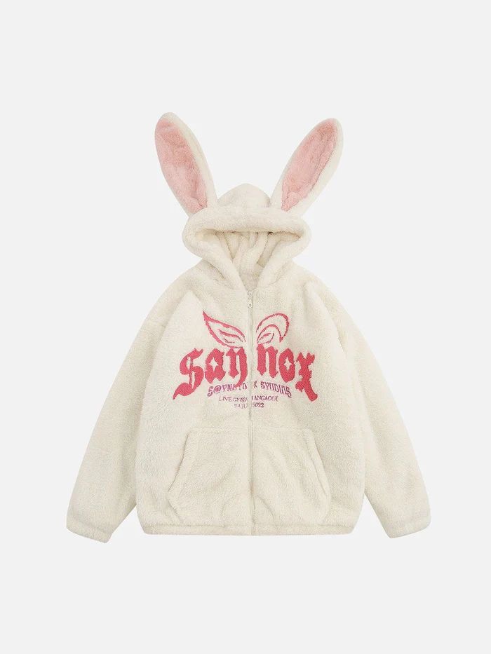 a white fuzzy hoodie with pink bunny ears on the hood.  the hoodie has a zip up closure and a graphic logo embroidered on the chest. the hoodie is oversized and has a casual streetwear aesthetic.