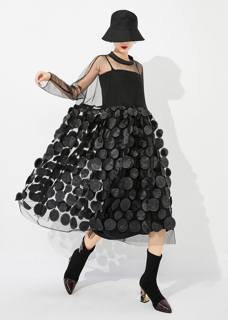 a woman in a black polka dot tulle dress and black boots poses in a studio against a white background. she is wearing a black hat and has a red lip.