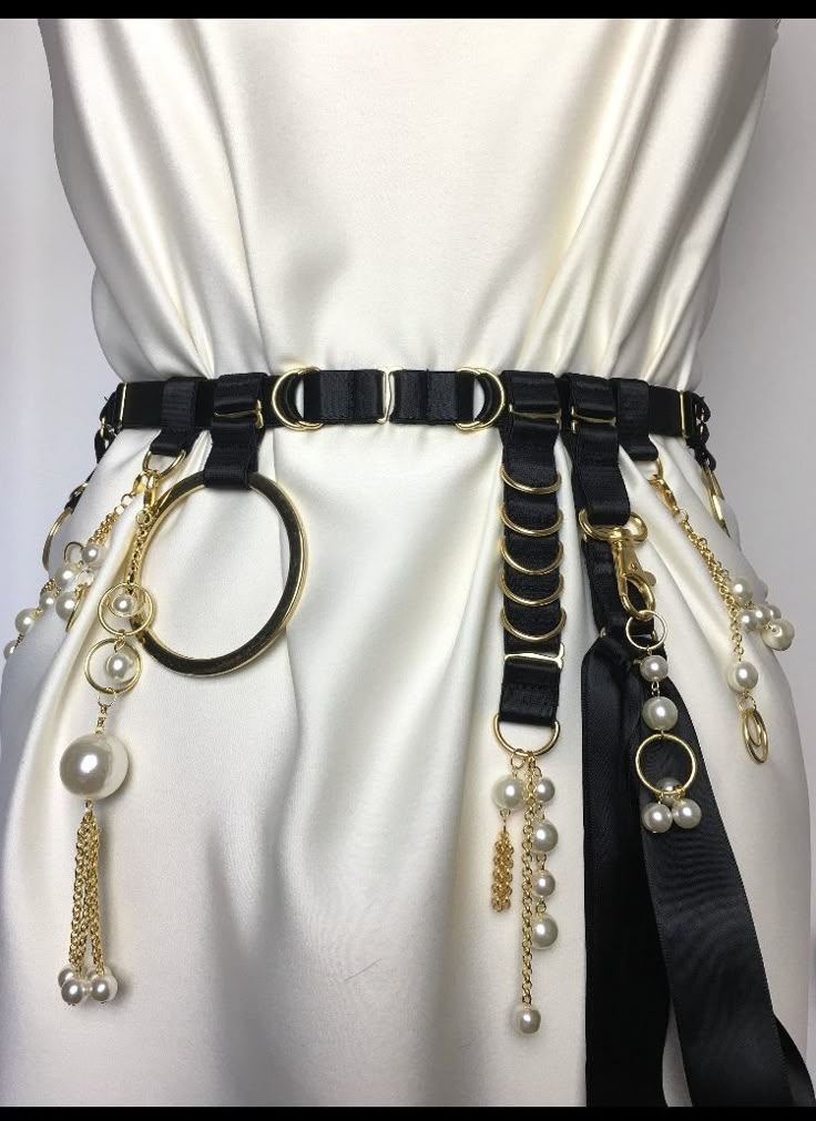a white dress is adorned with a black belt featuring gold rings, pearl embellishments, and hanging chains. the belt adds a stylish and decorative touch to the dress.