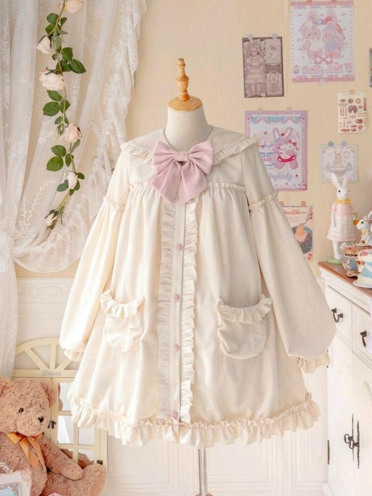 the image showcases a charming offwhite lolita fashion dress displayed on a mannequin. the dress boasts a peter pan collar adorned with a delicate pink bow. it features long sleeves, a buttondown front, and a flowy, ruffled skirt. two functional pockets grace the front, adding a touch of practicality to the whimsical design. the dress exudes an aura of delicate femininity and vintage charm, perfectly embodying the sweet lolita aesthetic. the setting is bright and airy, further enhancing the dress's ethereal beauty.