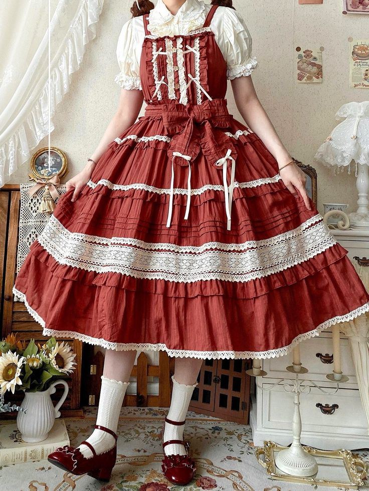 a person is standing in a room wearing a red tiered lolita fashion dress. they are also wearing a white blouse with a peter pan collar, white socks, and red mary jane shoes.  the dress has lace detailing along the layers of the skirt and features several bows made from a matching ribbon. the photo is taken at eye level in soft natural light.