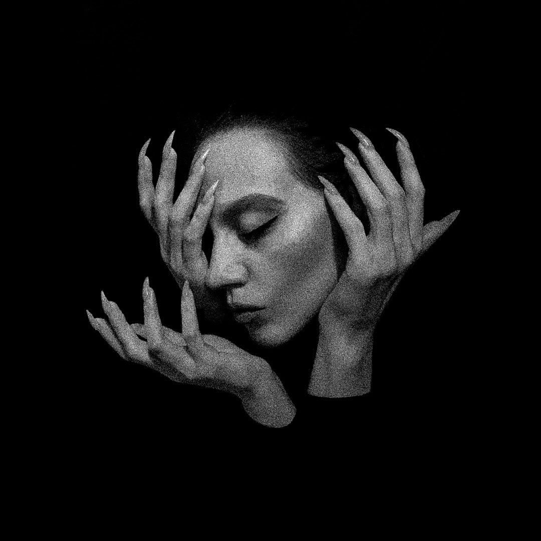 a black and white portrait of a woman with her hands covering her face. her fingers are long and thin, and her eyes are closed. the image is dark and mysterious, with deep shadows around her face.