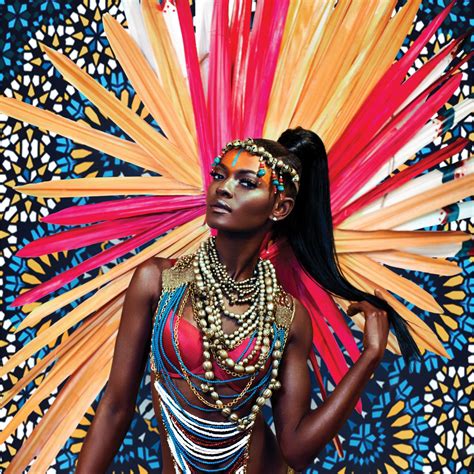 this is a portrait of a young black woman wearing a bright and colorful carnival costume. the woman is striking a pose and looking directly at the camera with a confident expression. she is adorned with elaborate jewelry, a headdress of red and yellow feathers, and bold makeup. the background is filled with a geometric design of blue, yellow, and green. the overall image is vibrant, festive, and full of energy.