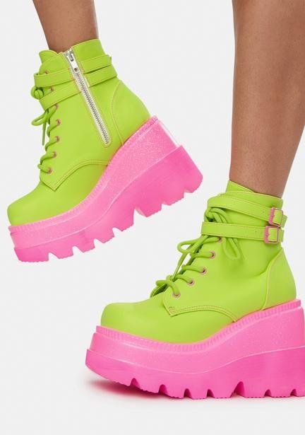 the image showcases a pair of neon green and pink platform ankle boots worn by someone. the boots are a bold and eyecatching fashion statement with a bright neon green upper and a thick, pink platform sole.