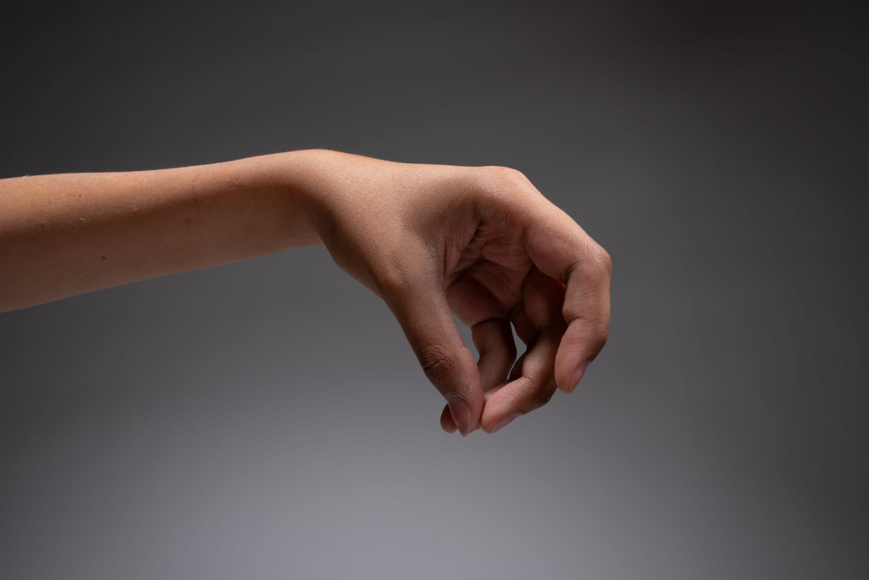 a person's hand extended forward, demonstrating a picking or grabbing gesture against a neutral gray background.