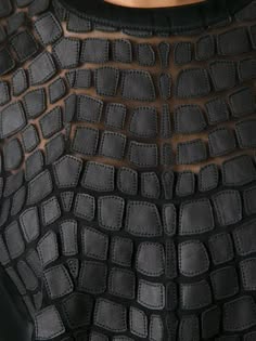 close up shot of a black, textured, leather fabric that appears to be a top. the fabric has a unique design that resembles crocodile scales. the texture is very detailed.