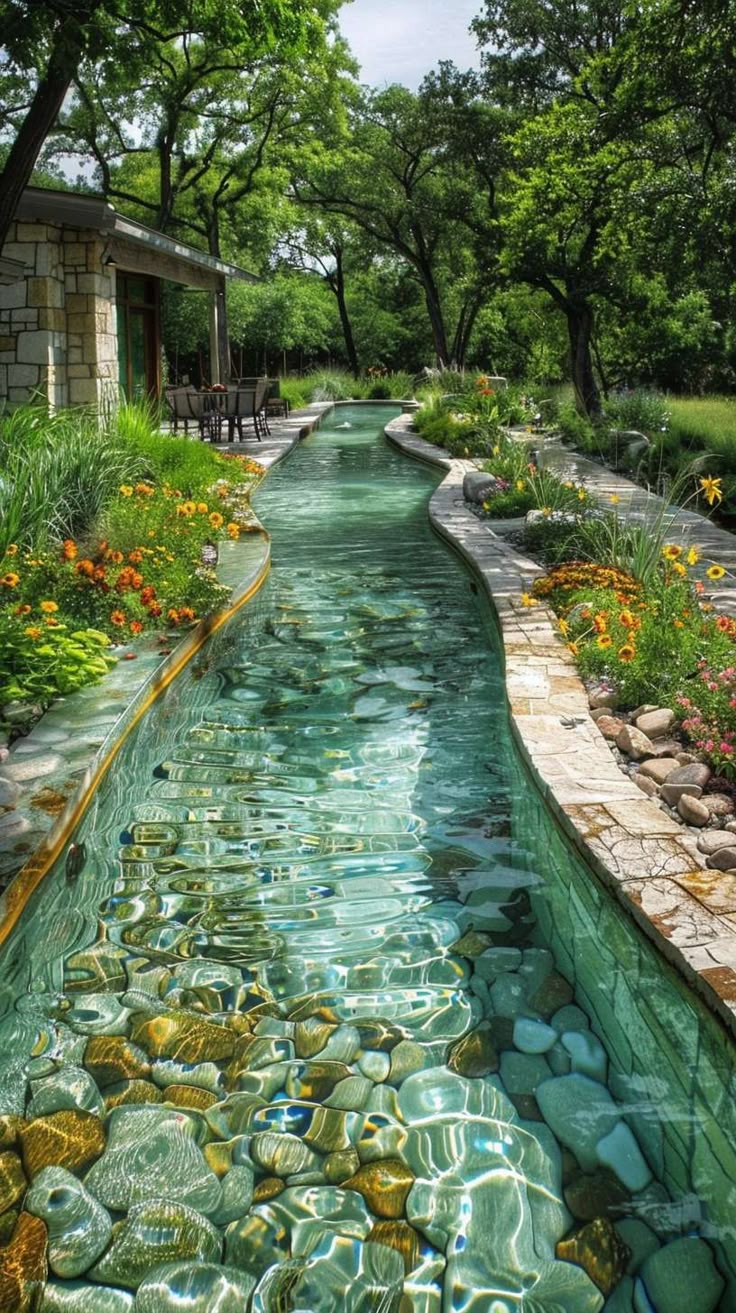 the image shows a long, winding stream flowing through a garden. the stream is filled with clear water and rocks. on either side of the stream are lush plants and colorful flowers. in the background, there is a house and several trees. the scene is peaceful and serene, capturing a welldesigned and maintained outdoor space.
