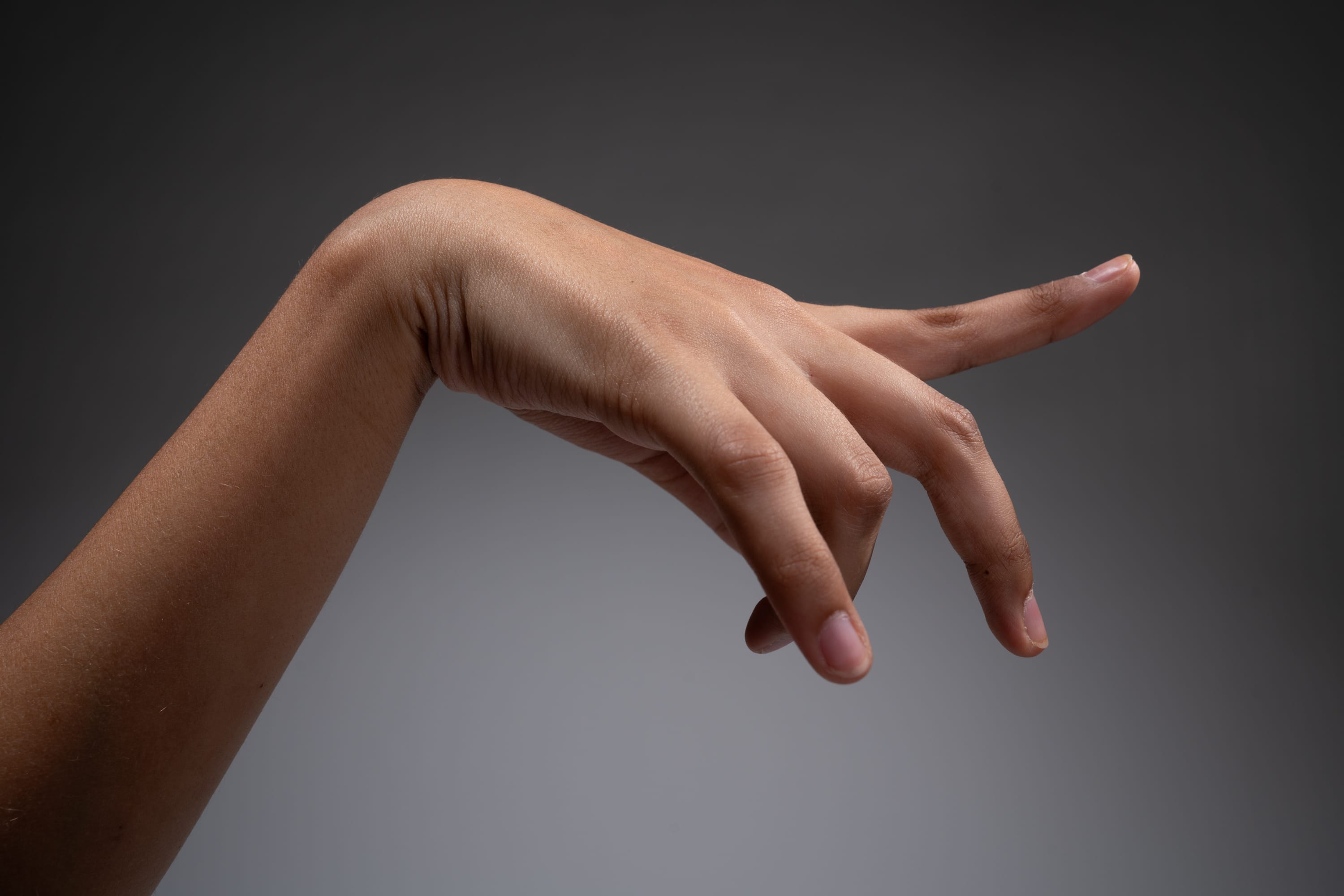 a closeup side view of a left hand with an extended index finger against a gray background.
