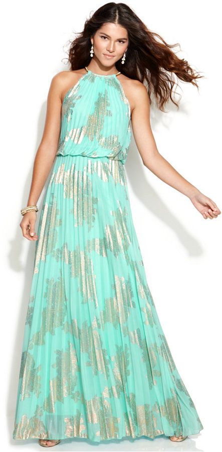 a beautiful woman in a blue and gold floral maxi dress. she has long, wavy hair and is wearing gold jewelry and earrings. she's smiling slightly and looking at the camera.