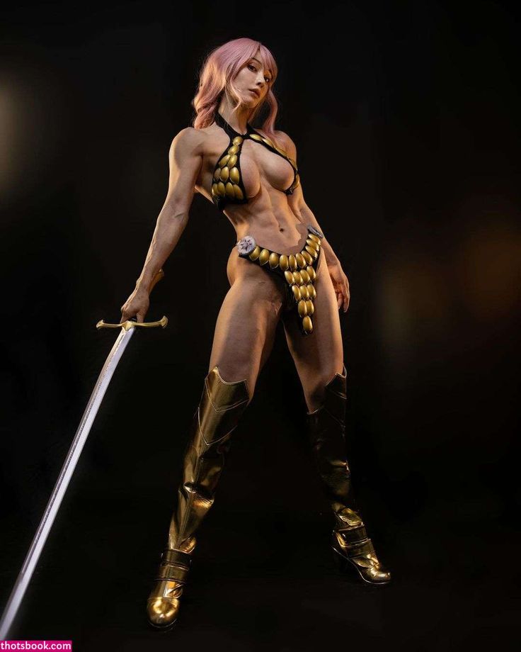 a woman with pink and blonde hair wearing a fantasy warrior costume, including armor, boots, and a sword, poses against a dark background. she has a muscular and athletic physique with visible abs. the low angle shot emphasizes her strength and costume.