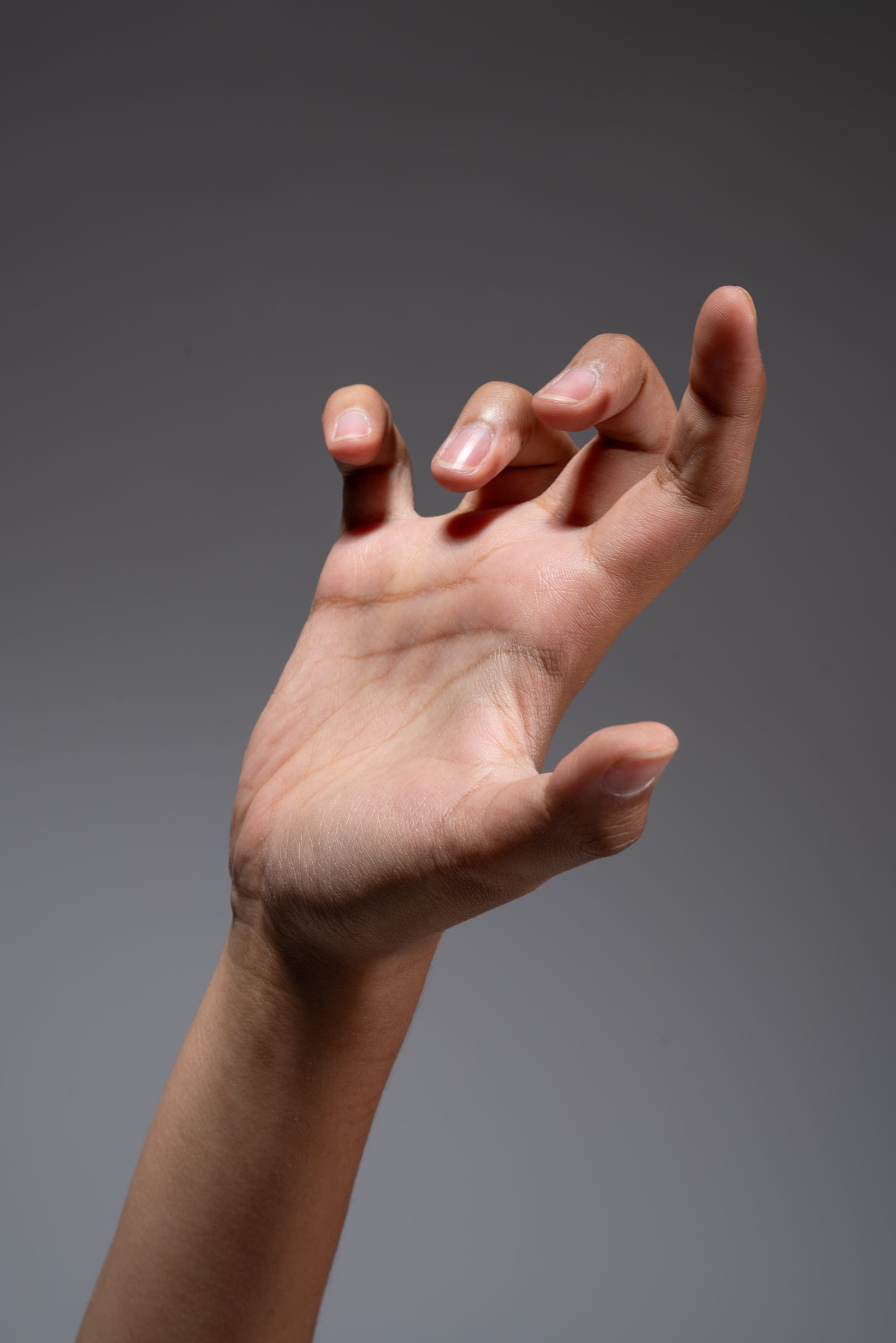 the image shows a closeup of a hand reaching forward with fingers extended as if grasping at something. the hand is illuminated with studio lighting against a gray background.