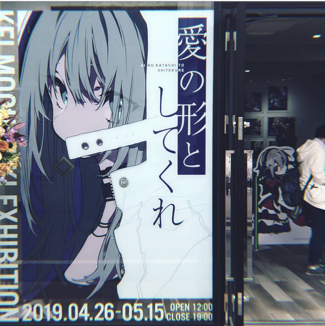 poster of an anime girl advertising an art exhibition. the poster is located in front of a shop and people are walking by.