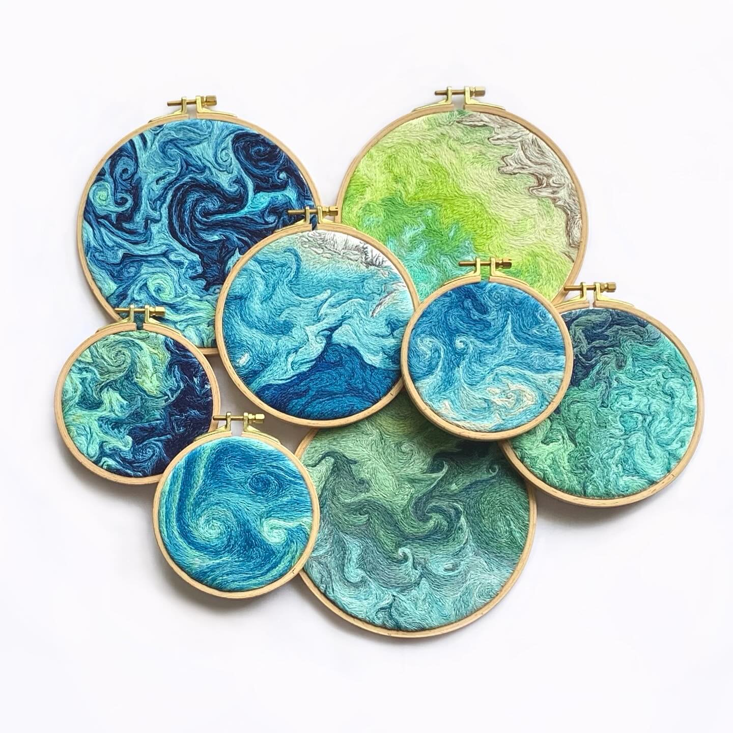 the image showcases a captivating collection of seven embroidery hoops, each adorned with intricate thread paintings that evoke the mesmerizing beauty of ocean waves. the hoops, in varying sizes, are artfully arranged, creating a visually dynamic composition.  the skillful use of thread creates a sense of depth and movement, mimicking the ebb and flow of water. the color palette is a harmonious blend of blues, greens, and white, capturing the tranquility and vibrancy of the ocean.