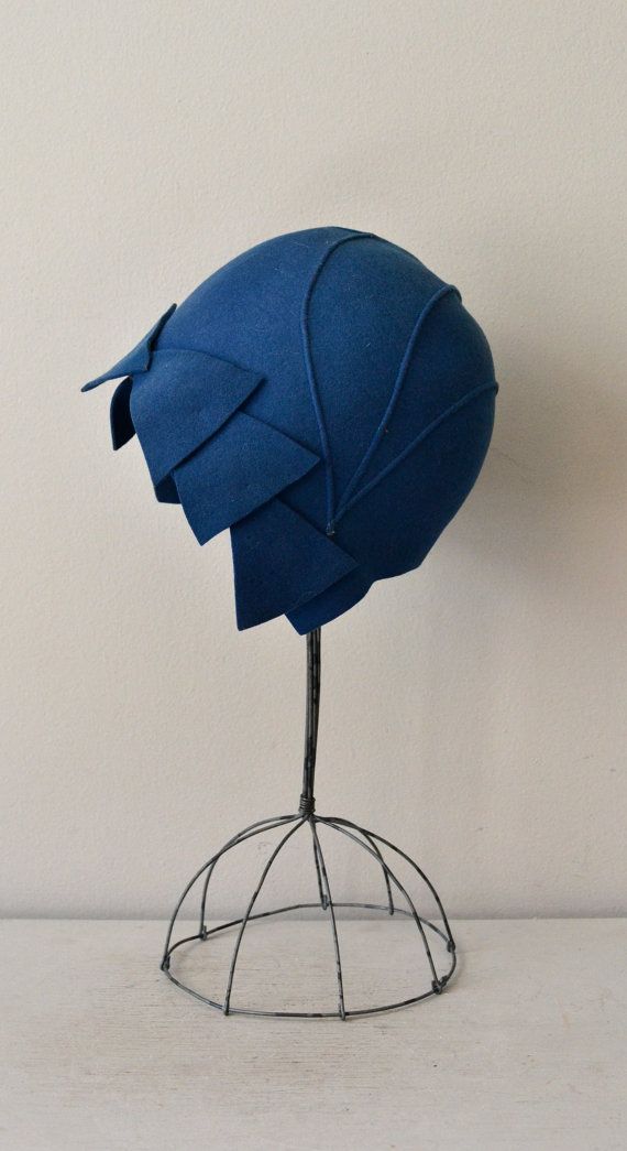 a blue cloche hat with a wire hat stand on a white background. the hat is made of felt and has a geometric design. the stand is made of wire and has a dome shape.