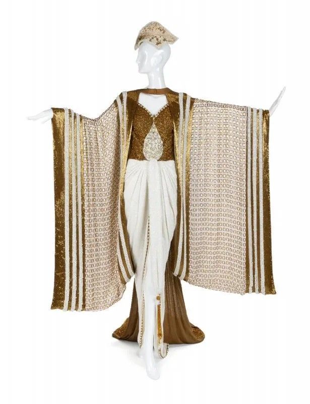 a mannequin is wearing a white and gold dress with a matching hat. the dress has a long, flowing skirt and sleeves.