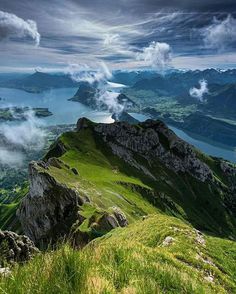 the image is an aerial view of a mountainous landscape. in the foreground is a lush green mountain with rocky cliffs. in the background, there are several lakes surrounded by mountains and valleys. the sky is cloudy with patches of blue.