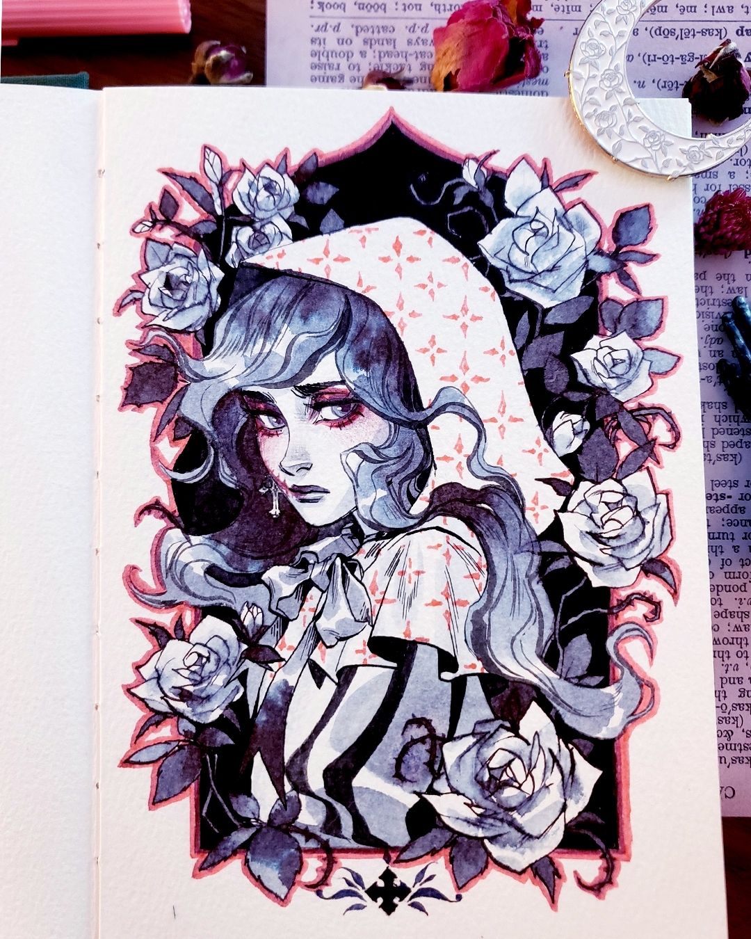 the image is a closeup shot of a detailed watercolor and ink illustration in a sketchbook. the artwork depicts a young woman with long dark hair, wearing a hooded cloak patterned with a faint geometric design. she has a melancholic expression and is surrounded by a profusion of dark, richly colored roses. the overall style is gothic romantic, blending dark and light elements with a vintage aesthetic. the artist has employed meticulous detail and shading to create a visually striking and emotionally evocative piece.  the sketchbook paper and surrounding objects are partially visible in the photograph.