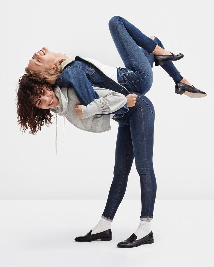 two women are wearing jeans and black loafers while playfully laughing. one woman is holding the other on her back.