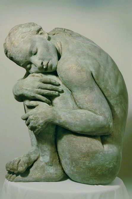 a sculpture of a female nude sitting in a curled up position with her chin on her knees and her hands clasped together. the sculpture is made of bronze and is painted in a green patina. the sculpture is very realistic and detailed, with smooth skin, visible hair, and veins. the sculpture depicts the subject as being deeply contemplative and sorrowful.