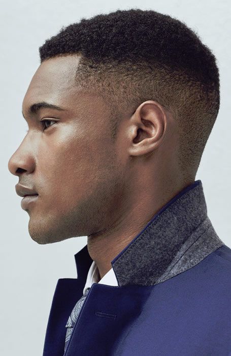 a profile view of an african american man with a short, faded haircut. he is wearing a blue suit with a gray collar, a white dress shirt, and a patterned tie. he is clean shaven and has light skin.