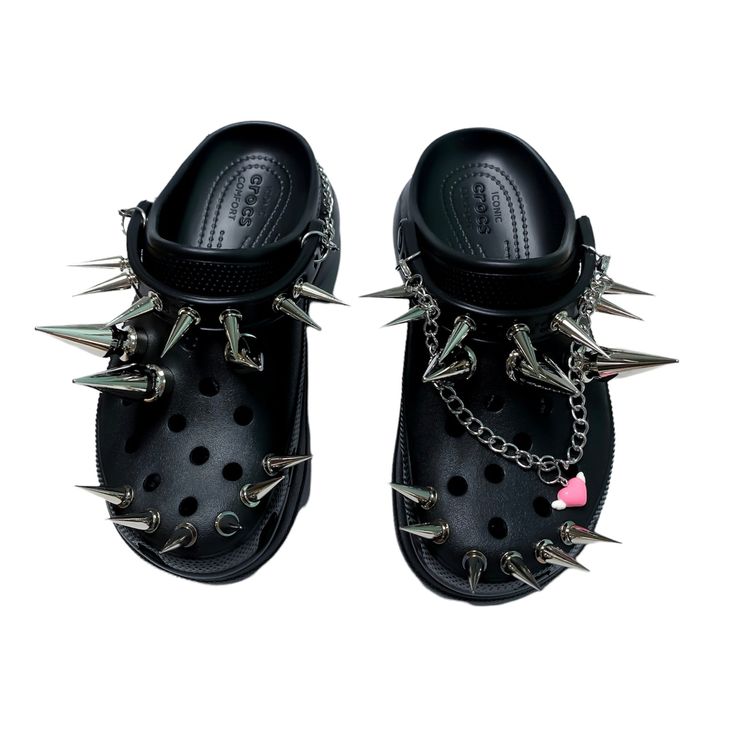 a pair of black crocs shoes with silver spikes and chains. they are adorned with a pink heart charm.