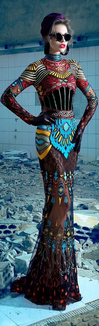 a woman with a striking dark hairstyle, sunglasses, and a bold red lip is modeling a fabulous patterned dress. the dress is black and white with hints of blue, yellow, and red, with a striking geometric pattern. she's standing in a grungestyle setting, with concrete flooring and a white backdrop. the dress has a  fitted silhouette with a long skirt. this image captures a unique and powerful fashion moment.
