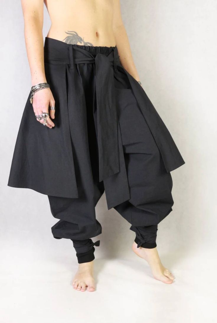 a man is wearing a black, wideleg, loosefitting pant with a matching black belt. the pants appear to be made of a soft, comfortable fabric and are designed with a relaxed fit. the pants have a flowing, almost kimonolike appearance, making them perfect for creating a modern, trendy streetwear look. the model is barefoot and has a casual, relaxed look.