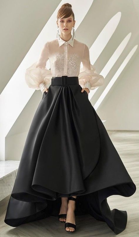 a woman in a white shirt and black highlow skirt stands in a studio, posing for the camera. her look is elegant and sophisticated, perfect for a formal event. she is wearing accessories such as earrings and a belt, and her shoes are high heels.  the background is white, creating a clean and simple backdrop for the model's outfit.