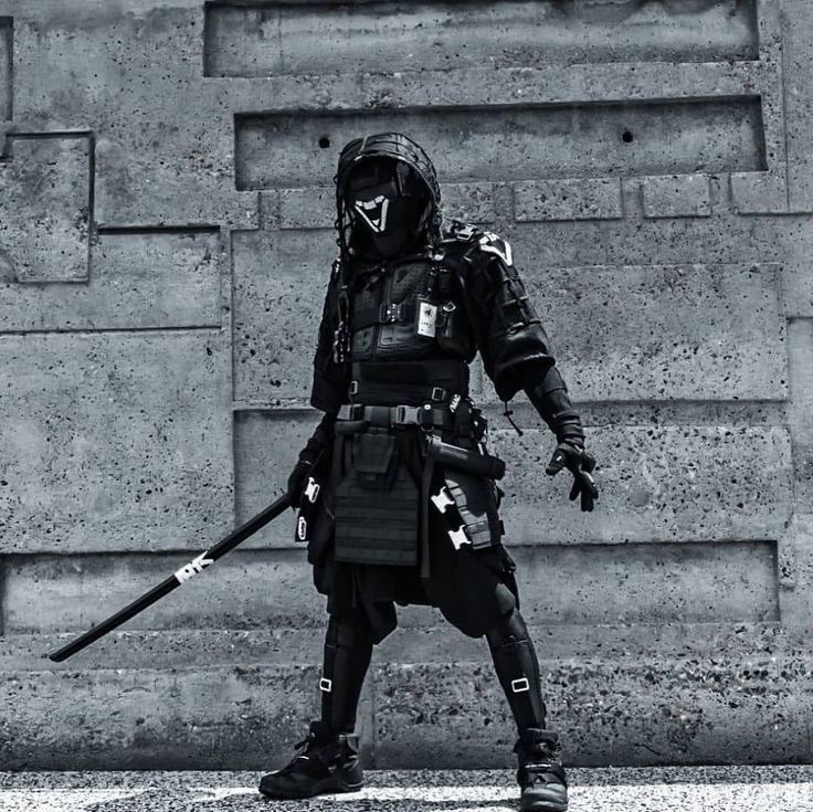 a person dressed as a modern samurai in black tactical gear with a mask and a katana sword. the person is standing against a concrete wall, the image is taken in a urban setting, showing the contrast between traditional samurai attire and a futuristic, cyberpunkesque style.