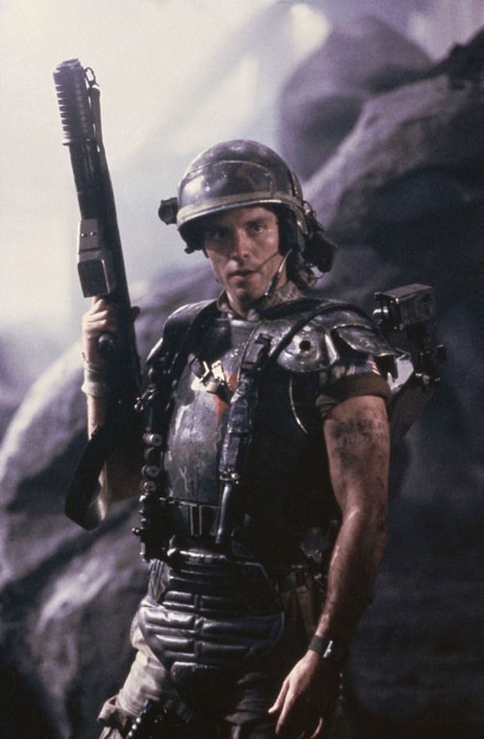 a closeup of a space marine soldier wearing a helmet and wielding a rifle. the marine is in combat gear and stands in a shadowy, ominous environment, suggesting a scene from a science fiction movie.