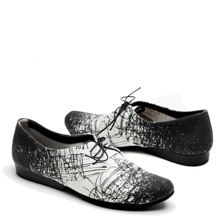 pair of black and white women's oxfords with an abstract, scribbled print are shown. the shoes are laceup and have a flat sole. one shoe is positioned slightly ahead of the other, showcasing the design details. the background is plain white, ensuring the focus remains on the shoes. the overall style appears to be both casual and stylish, blending comfort and fashion.