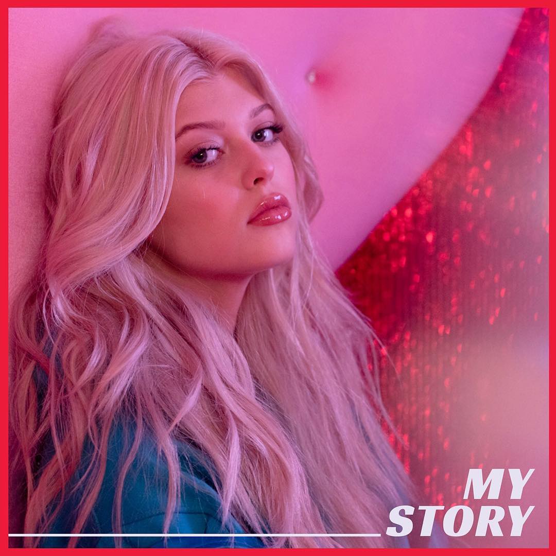 a portrait of a young woman with long, flowing blonde hair, wearing glossy lip makeup and blue clothing. she is posed against a pink backdrop in a studio setting. the text "my story" is visible at the bottom right corner of the image. the overall aesthetic is glamorous and fashionable, suggesting the image might be related to music or a personal story.