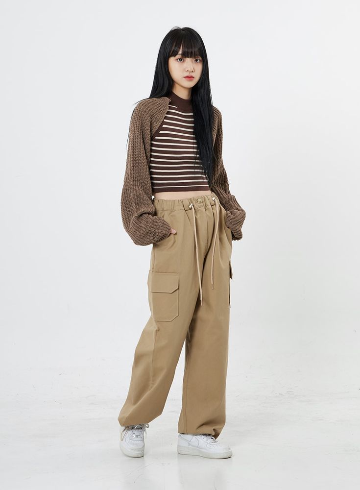 a young woman poses in a studio against a white background, showcasing a stylish casual outfit. she's wearing a brown striped cropped top, a brown knit cardigan, and beige cargo pants. her footwear consists of white sneakers. the overall aesthetic leans toward trendy korean street style.  the image is welllit, and the focus is sharply on the model.