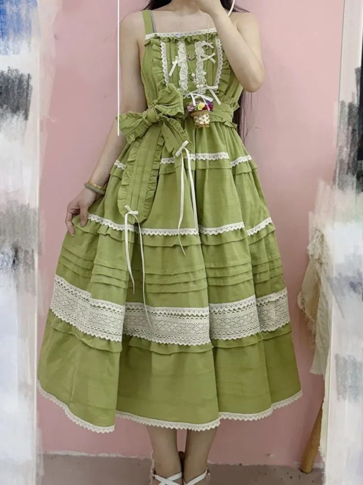 a woman is modeling a flowing green dress. the dress has lace trim and a tiered skirt. the dress is sleeveless and has a sweetheart neckline. the model is wearing her hair down and has on minimal makeup. she is standing in front of a pink background.
