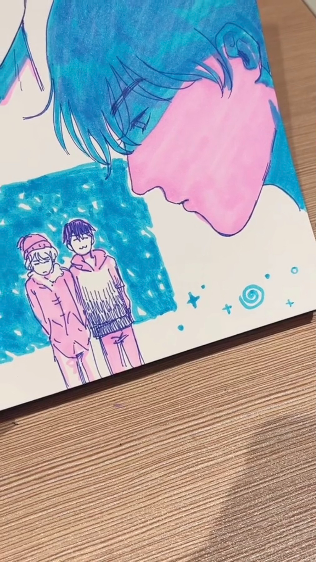 the image is a digital scan or photograph of a sketchbook page featuring several anime or mangastyle illustrations drawn in colored markers. the most prominent drawing is a closeup of a boy with blue hair and pink skin, his eyes closed as if he's sleeping or lost in thought. the style suggests a dreamy or emotional atmosphere.  below this main figure is a smaller drawing of two boys standing together against a blue background with white dots, possibly representing snow. one boy has black hair and a pink hoodie, while the other has white hair and a pink jacket. the presence of sparkles and a spiral doodle around the main figure adds a touch of whimsy and suggests a possible romantic connection between the characters.
