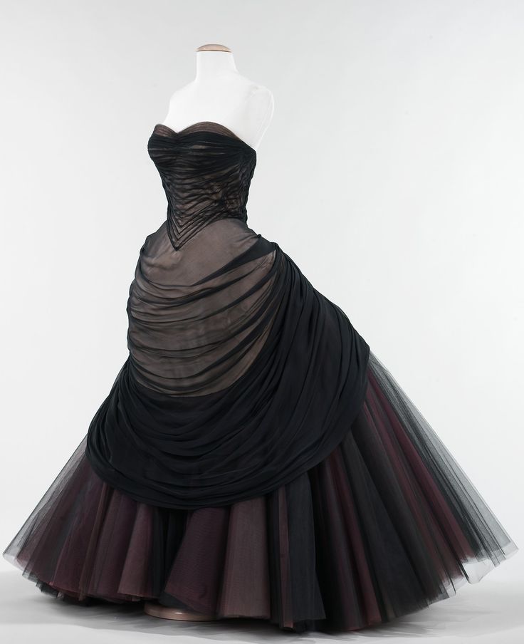 a formal gown is displayed on a mannequin. the dress is strapless with a brown bustier, draped with black tulle, and a full tulle skirt with layers of black and brown tulle. the dress is set against a white background in a studio setting. the style suggests a vintage aesthetic.